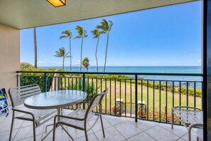 Un balcon avec vue sur l’océan, des palmiers et un sol carrelé.