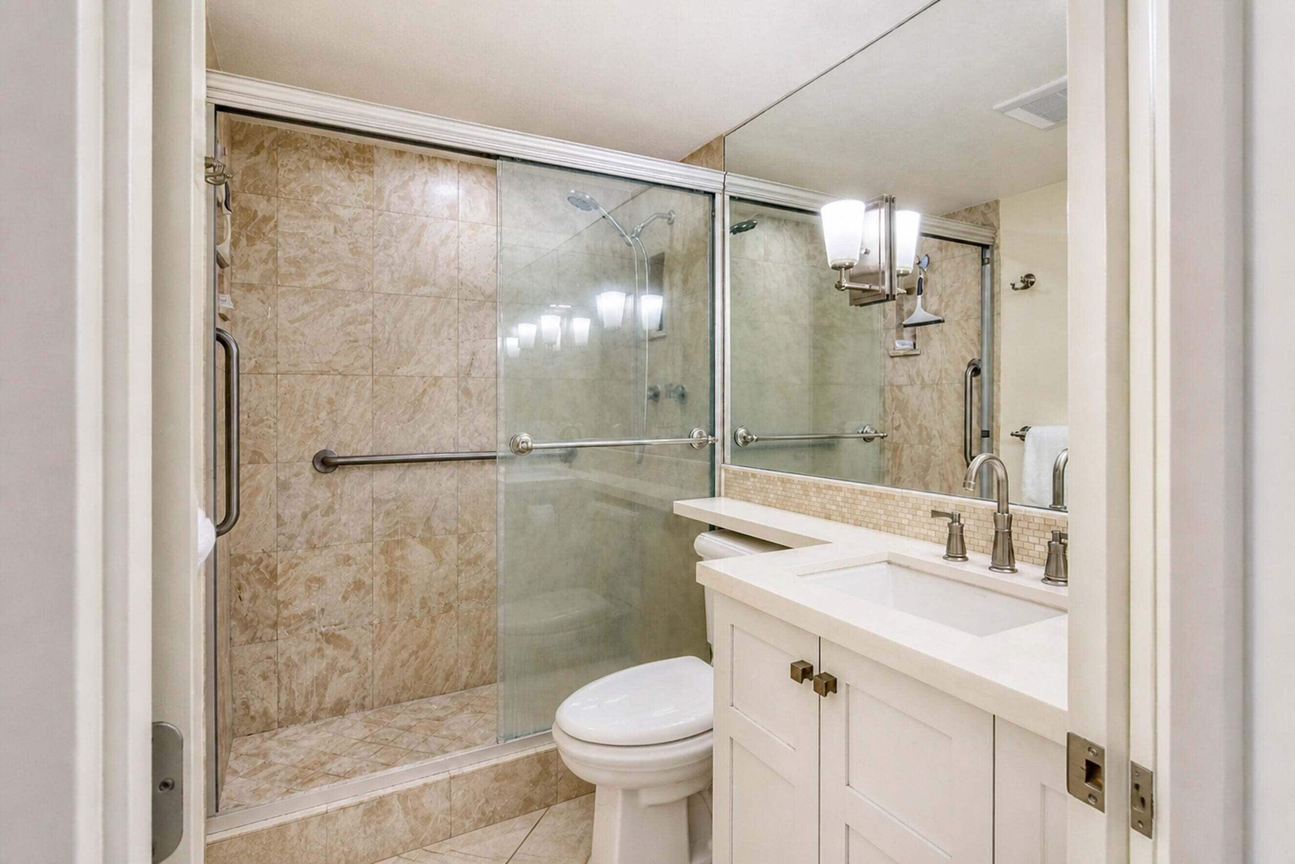A modern bathroom with a glass-enclosed shower, a white toilet, and a vanity with a mirror.