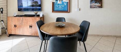 A dining area with a round wooden table, four black chairs, a wooden cabinet, a television, and two framed artworks on the wall.