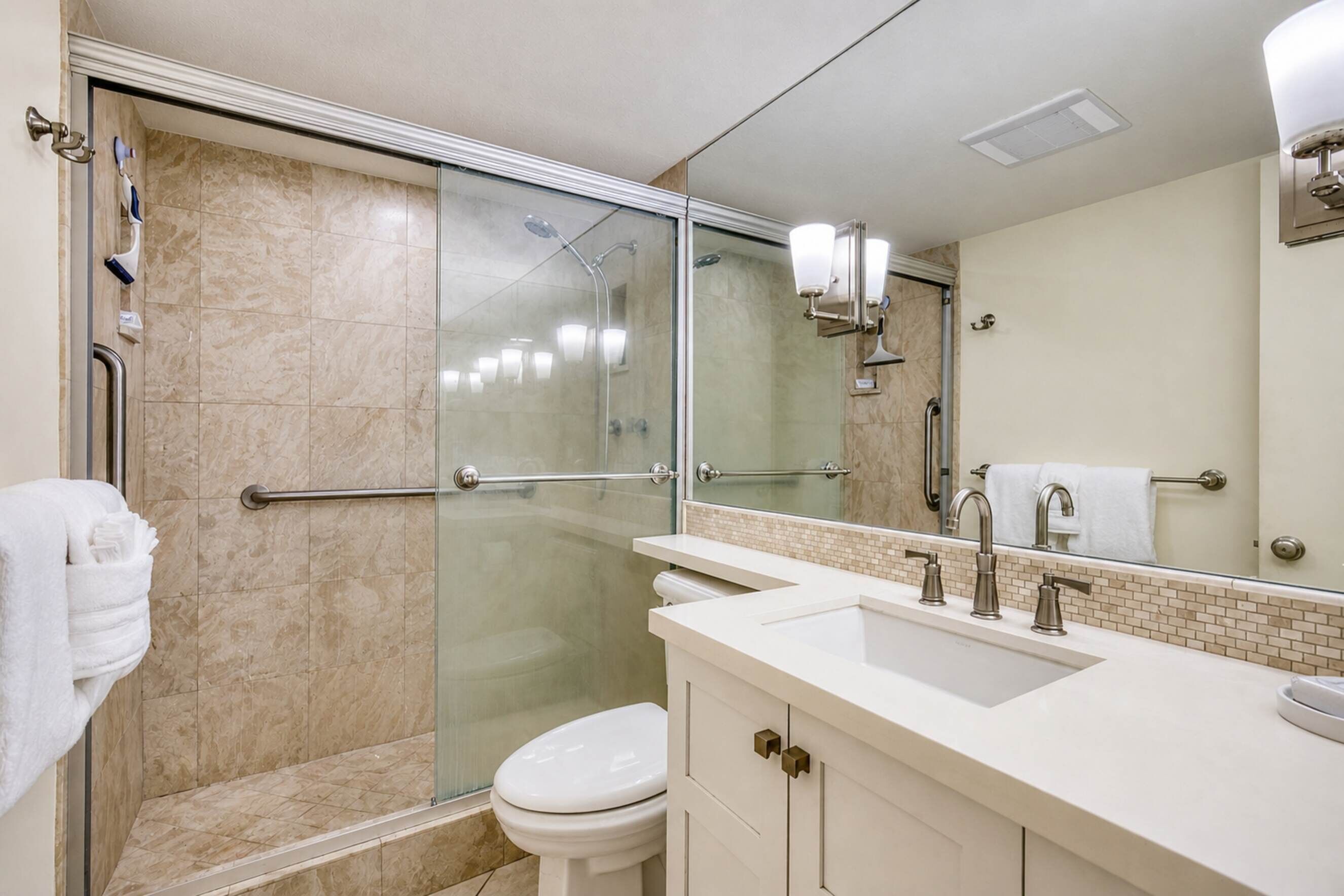A modern bathroom with a glass-enclosed shower, a white toilet, and a vanity with a sink and mirror.