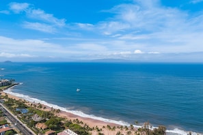 A coastal view with a beach, ocean, and a road leading to a residential area.