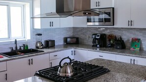 A modern kitchen with white cabinets, a stainless steel range hood, a gas stove, a blender, a toaster, and a coffee maker. - 2 bedroom 2 bathroom beach house, beach right at your door steps, (Steventon)