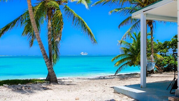 A beach with clear turquoise water, palm trees, and a white building with a covered patio. - 2 bedroom 2 bathroom beach house, beach right at your door steps, (Steventon)