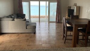 A living room with a sofa, a dining table with chairs, a ceiling fan, and a view of the beach through glass doors. - 2 bedroom 2 bathroom beach house, beach right at your door steps, (Steventon)