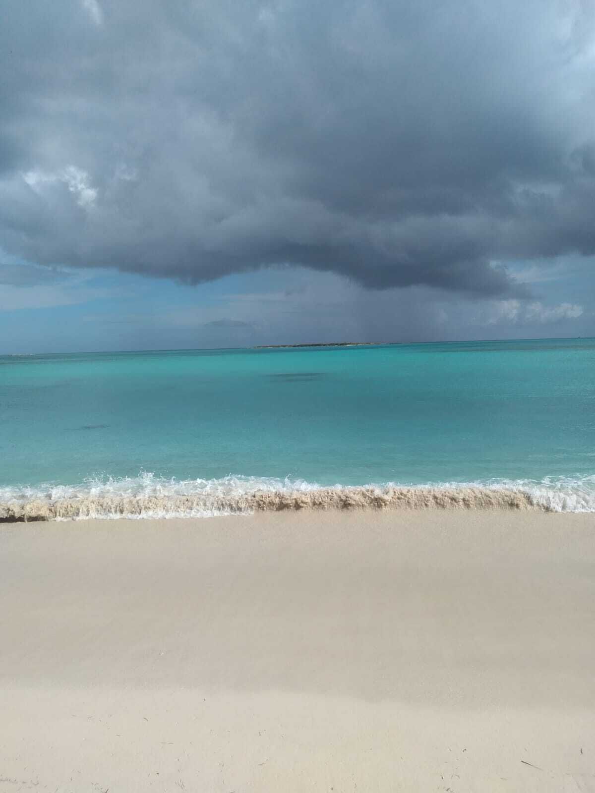 Une plage à l’eau turquoise et limpide, bordée d’un rivage sablonneux, sous un ciel nuageux.
