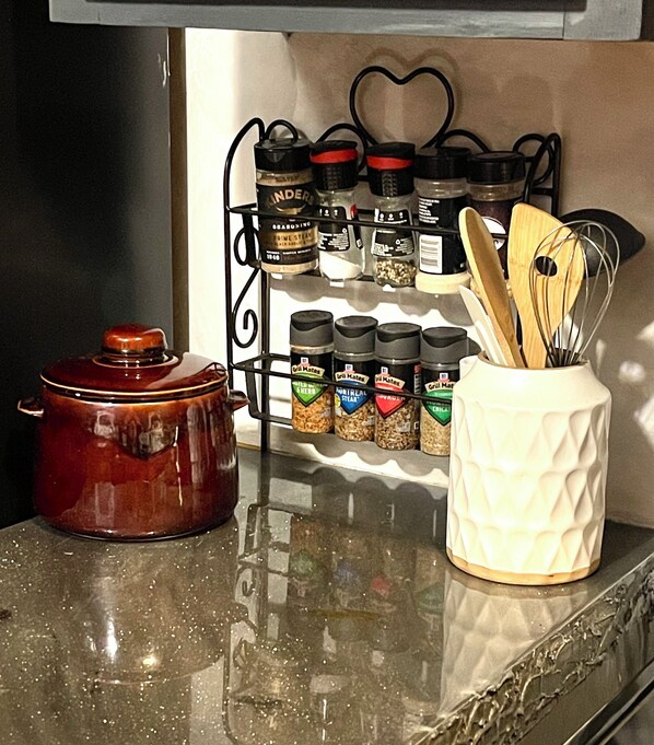 Una encimera de cocina con un especiero, una olla de hierro fundido y un recipiente de cerámica blanca que contiene utensilios de madera.