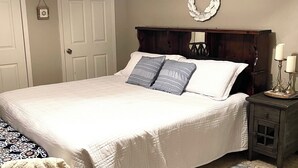 A neatly made bed with a white comforter and two pillows, a wooden headboard, a small bedside table with two candles, and a patterned rug on the floor. - Enjoy a cozy holiday getaway in our peaceful rural home.
WIFI NOT AVAILABLE (Mead)