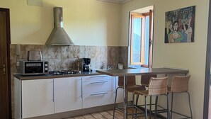 A kitchen with a gas stove, microwave, and a coffee maker. There are two bar stools and a window with a view. - Holidayapartments in beautiful house, private garden, free Wi-Fi (Tignale)