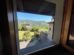 Blick aus einem Fenster auf eine gebirgige Landschaft mit einem Steinhaus und blauem Himmel.