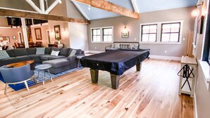 A spacious living area with a high ceiling, wooden beams, a pool table, and a seating area with sofas and a coffee table.