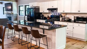 A modern kitchen with white cabinets, a large island with bar stools, a built-in oven, and a hanging light fixture.