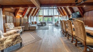 Ein geräumiger Loft-Raum mit hoher Decke, Holzbalken und großen Fenstern mit Blick ins Freie.