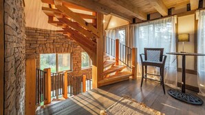 Eine Holztreppe führt zu einem Balkon mit einer Steinsäule, einem Tisch mit Stühlen und einer Lampe.