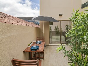 A balcony with a wooden table and chairs, a black umbrella, and a potted plant. - Building in the Funchal centre, Drapes Design (Funchal)