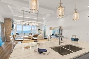 A spacious living area with a large marble island, a stone accent wall, and a view of the ocean. - Spacious Modern Condo in Door County w/ Spectacular Bay Views (Sister Bay)