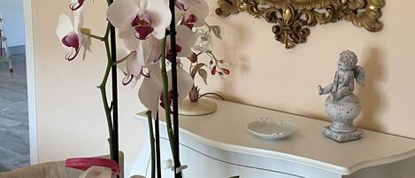 Una habitación con un tocador blanco, un espejo dorado ornamentado y orquídeas blancas.