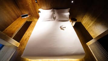 A neatly made bed with white linens and pillows, a bedside table with a smartphone, and a wall-mounted light fixture.