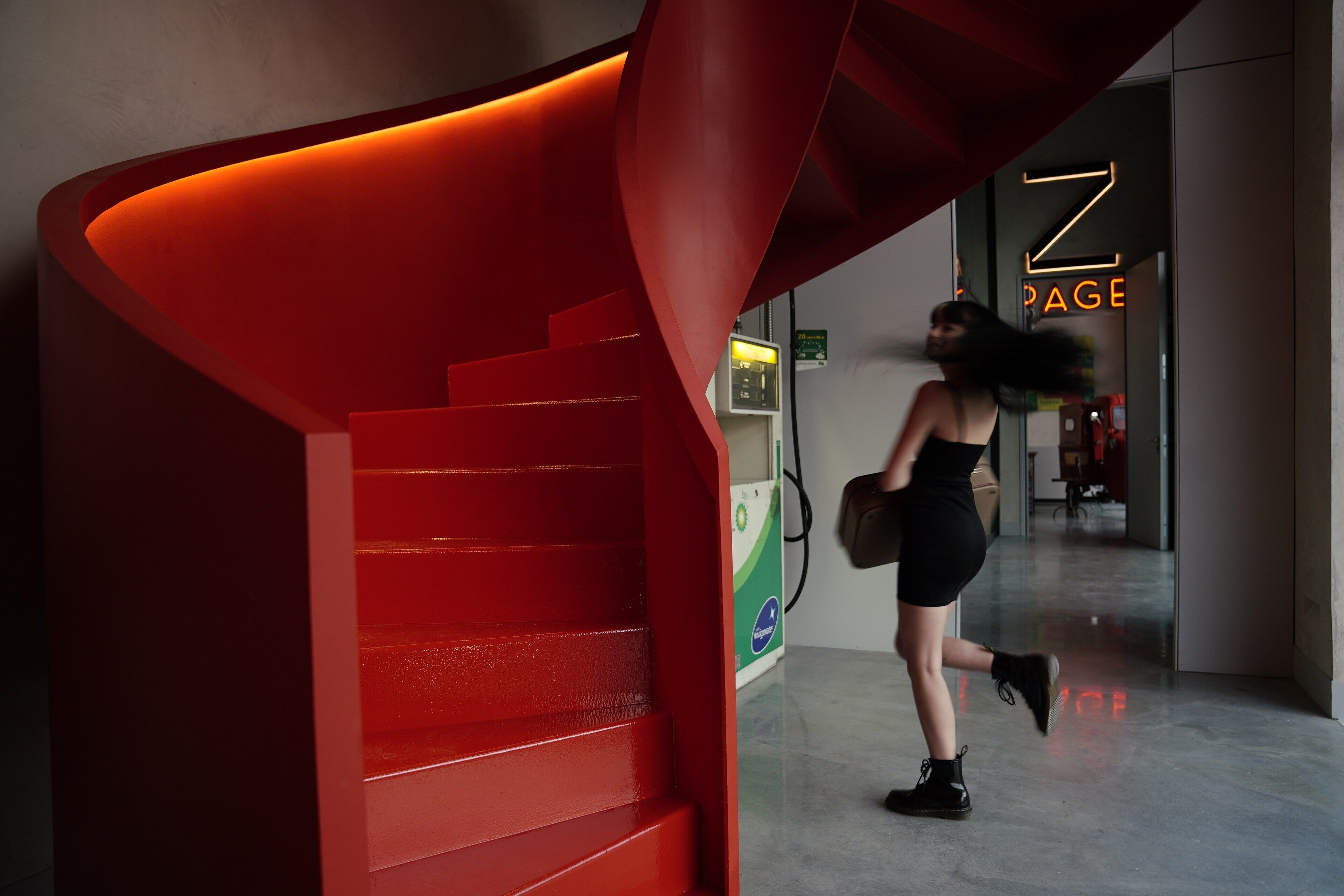 Un interior moderno con una escalera espiral roja y un letrero de neón que dice "Z PAGE".