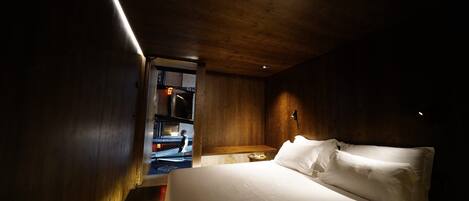 A bedroom with a large bed, wooden walls, and a small bedside table.