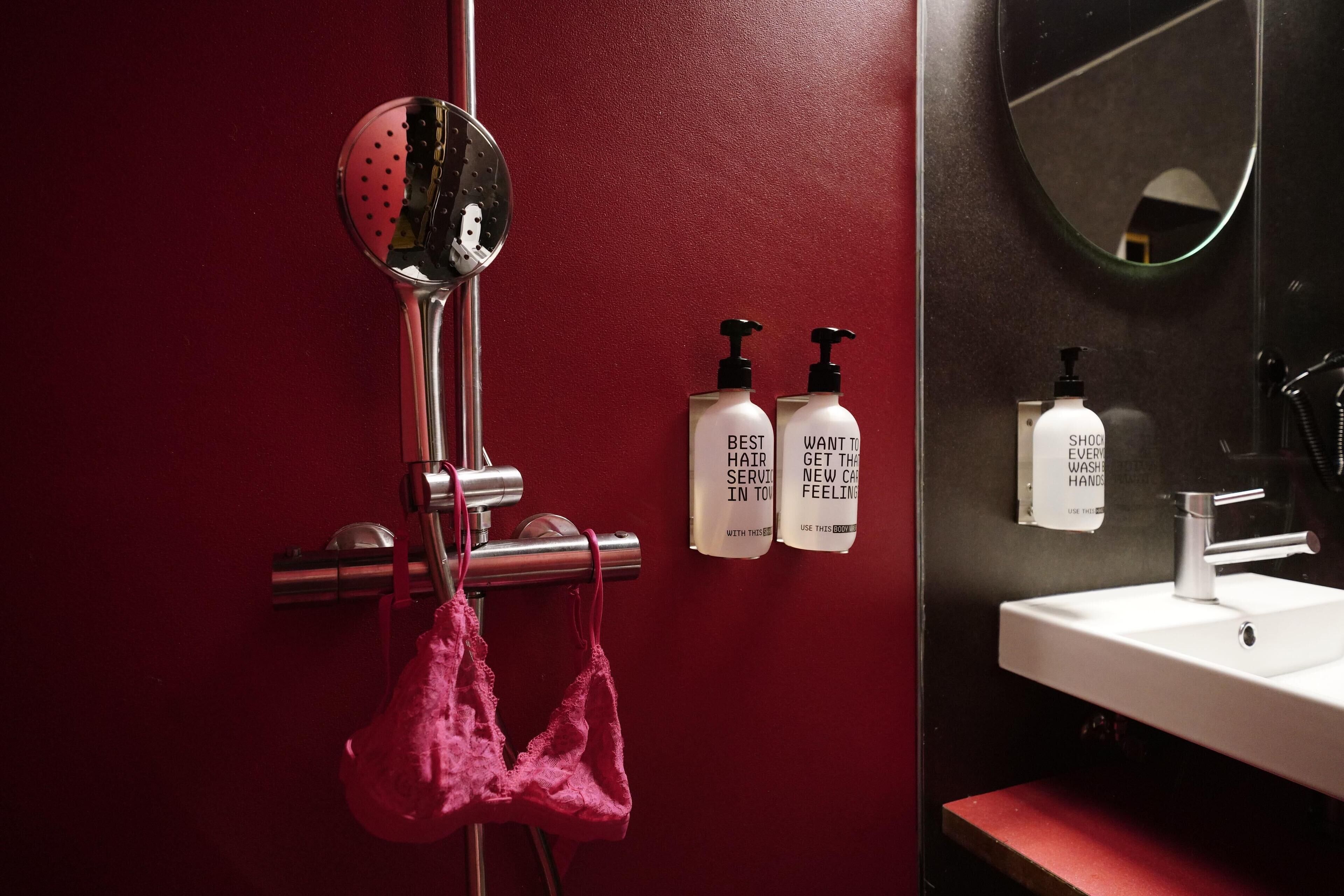 A bathroom with a red wall, a mirror, a sink, and two bottles of shampoo.