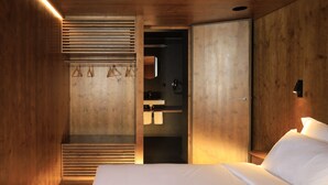 A modern bedroom with a wooden interior, a bed with white linens, a built-in wardrobe, and a small bathroom with a sink and mirror. - Zero Box Lodge Coimbra (Coimbra)