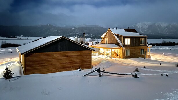 A wooden cabin with a large barn, a covered porch, and a view of snow-covered mountains in the background. - MODERN RUSTIC CABIN WITH WATER ACCESS AND BOAT DOCK [SLEEPS 17] (West Yellowstone)