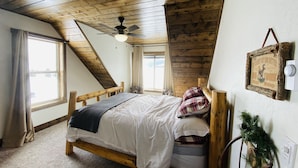 A bedroom with a sloped ceiling, a bed, a ceiling fan, a window, and a wall-mounted light switch. - MODERN RUSTIC CABIN WITH WATER ACCESS AND BOAT DOCK [SLEEPS 17] (West Yellowstone)