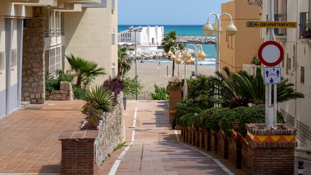 Een pad dat naar een strand leidt, met een bordje voor 'JSM Apartamentos'.