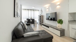 Een moderne woonkamer met een donkere bank, een flatscreen-televisie en een minimalistisch ontwerp.