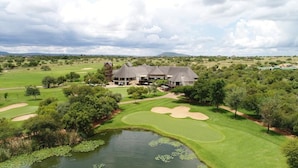 A golf course with a clubhouse, a pond with lily pads, and surrounding greenery.