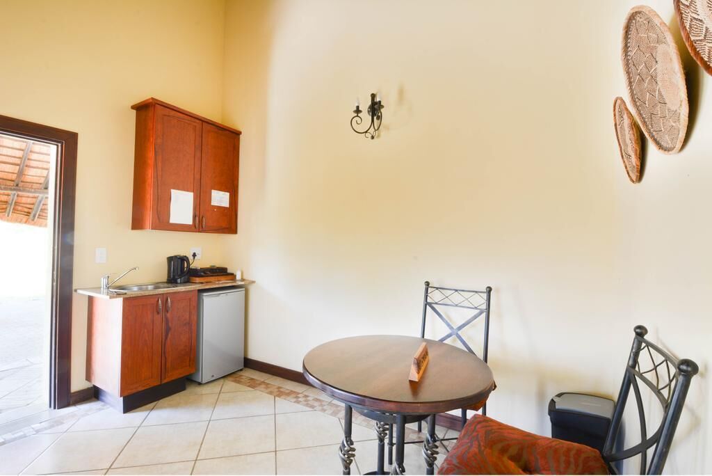 A compact kitchen with wooden cabinets, a sink, and a small refrigerator. There is a round dining table with two chairs and a single decorative item on it.