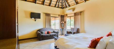 Habitación de hotel con cama, sofá, televisión y balcón con cortinas.