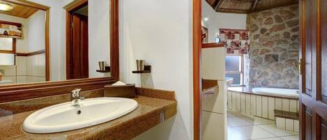 A bathroom with a granite countertop, a white sink, and a large mirror. There is a stone wall and a wooden door visible.