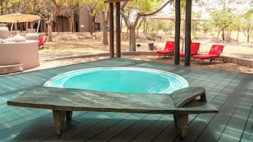 Una terraza de madera con un jacuzzi, sillas reclinables rojas y una pérgola.