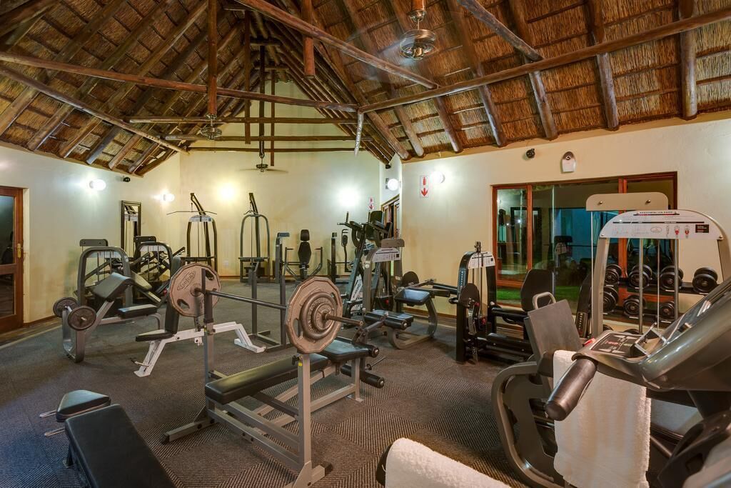 A gym with various exercise equipment, a thatched roof, and a mirrored wall.
