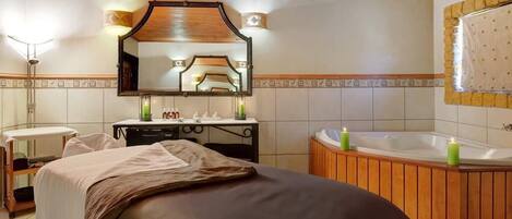 A bedroom with a bed, a vanity with toiletries, a large mirror, and a wooden bathtub.