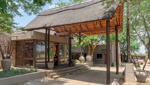 A covered outdoor area with a thatched roof, stone walls, and large planters.