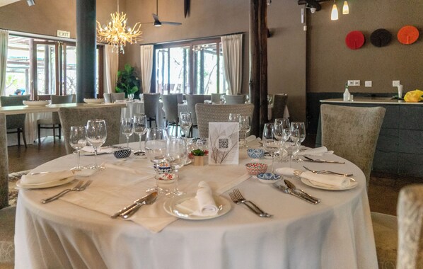 A restaurant with round tables set for dining, featuring white tablecloths, neatly arranged cutlery, and wine glasses.