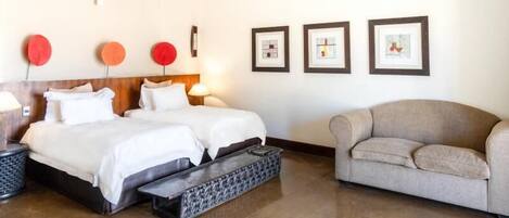 Habitación de hotel con dos camas, un sofá y cuadros en la pared.