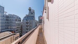 Un estrecho pasillo con paredes de baldosas y una barandilla de metal, que conduce a un edificio de varios pisos y una estructura distintiva en el techo.