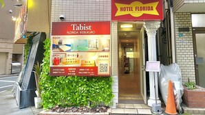 Un hotel llamado "Tabist Florida IKEBUKURO" con un toldo rojo, un cartel que muestra las características de las habitaciones y una pequeña entrada.