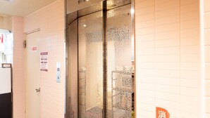 Un ascensor con puerta de vidrio, un letrero de alarma de incendios y un cartel con caracteres chinos.