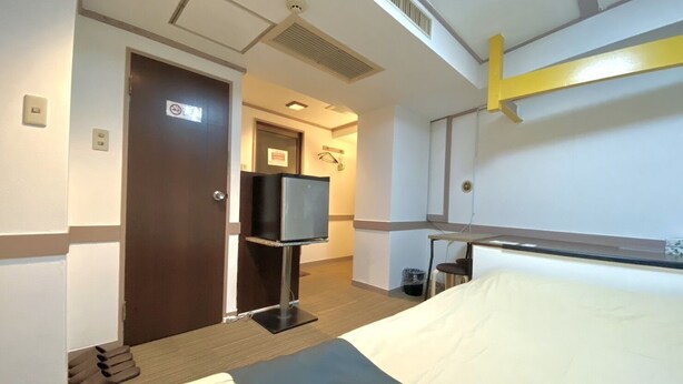 Una habitación de hotel con una cama, un televisor sobre un soporte, una puerta y una mesita.