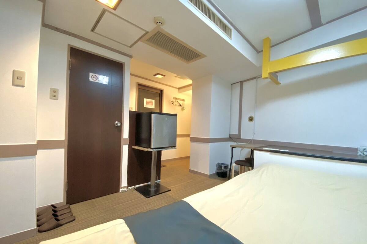 A hotel room with a bed, a television on a stand, a door, and a small table.