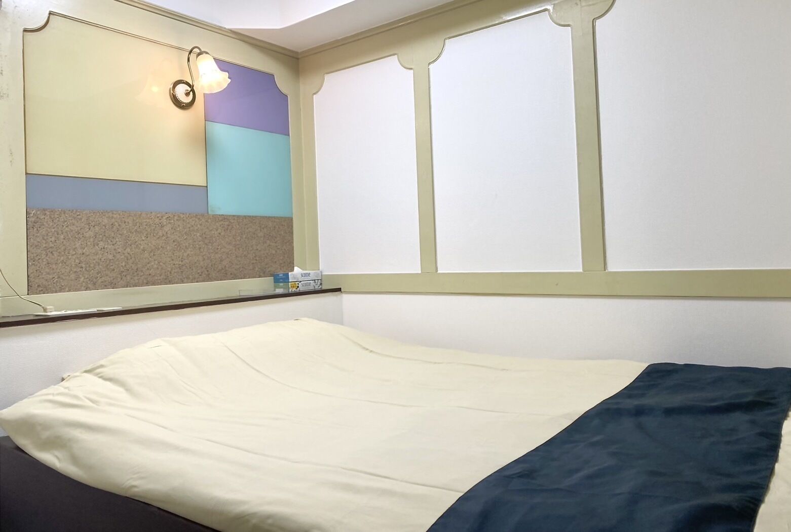 A single bed with a cream-colored mattress and a dark blue blanket. A small box labeled "SLEEPER" is on the nightstand.