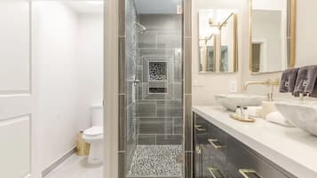 A modern bathroom with a glass-enclosed shower, a white toilet, and a vanity with two sinks and a large mirror.
