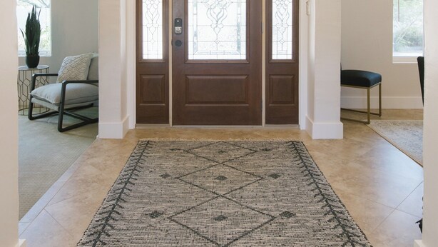 A spacious entryway with a patterned rug, a modern ceiling light fixture, and a double door with glass panels.