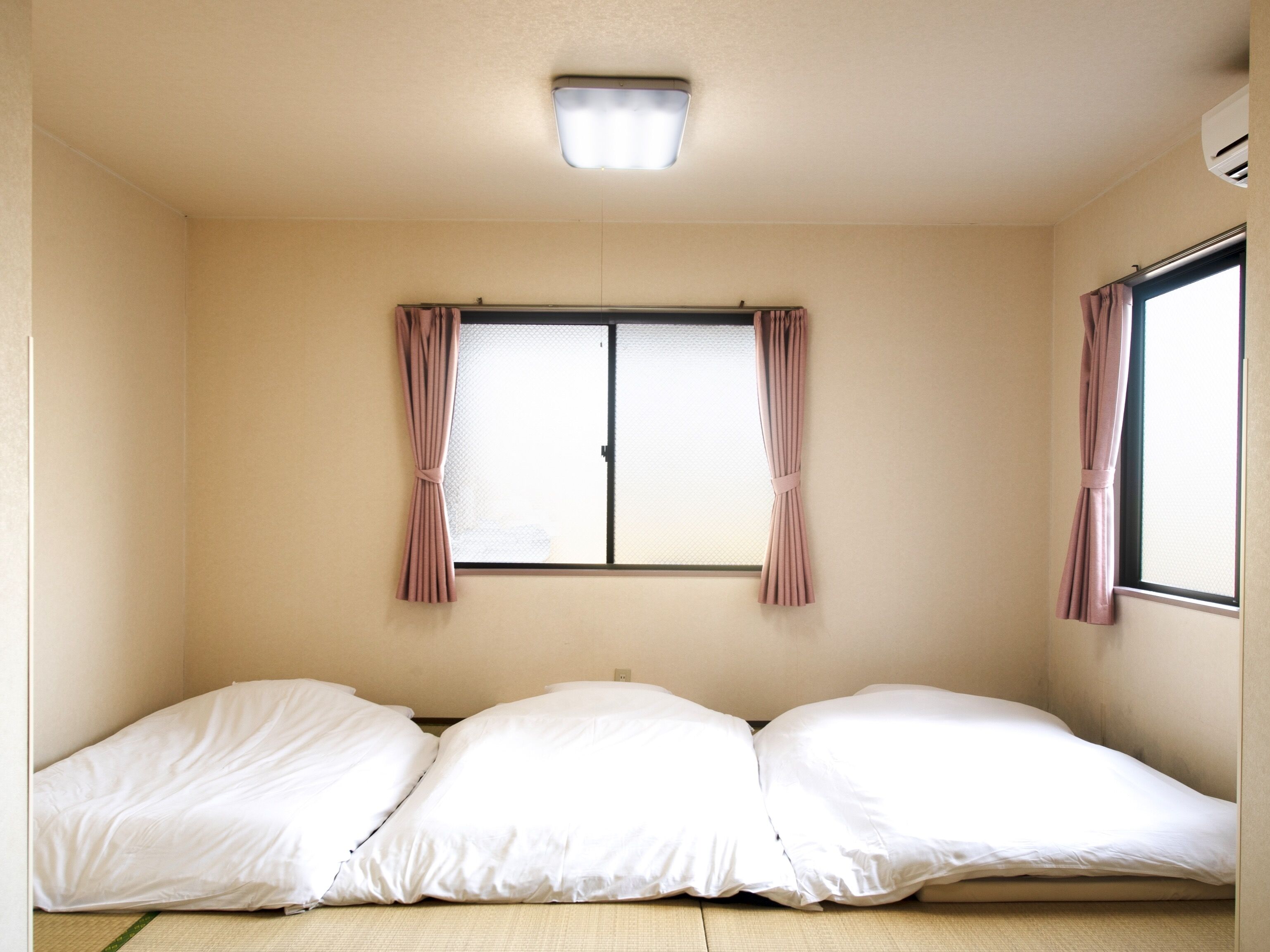 Une chambre avec un lit simple, une fenêtre avec des rideaux et un luminaire au plafond.