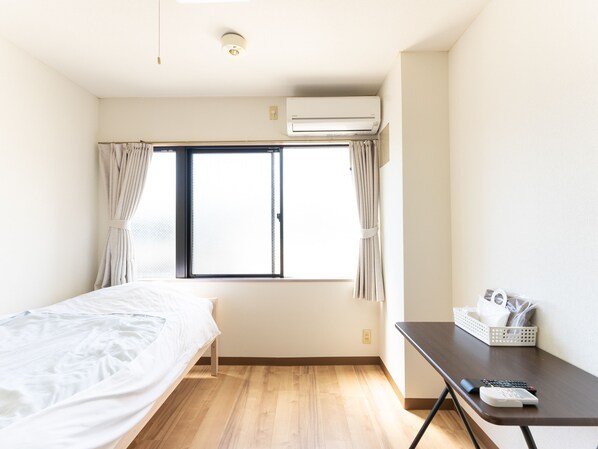 Habitación de hotel con cama, escritorio, ventana con cortinas, unidad de aire acondicionado y cesta de artículos de aseo.
