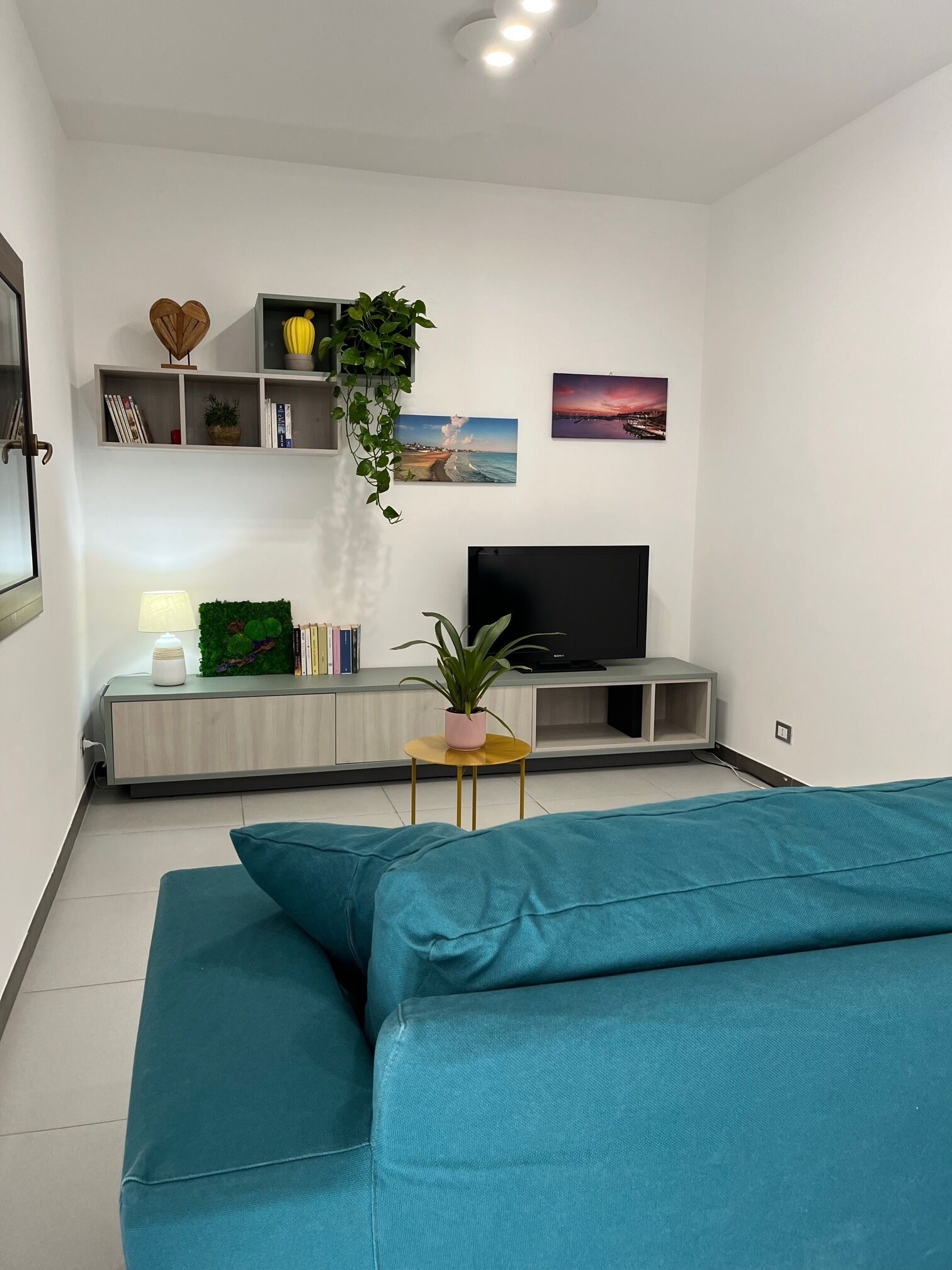 A modern living room with a large flat-screen TV, a sofa, a small side table, and a bookshelf with decorative items.